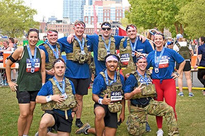 A group of friends posing on the grass with Carry Forward participation medals after a 5K.