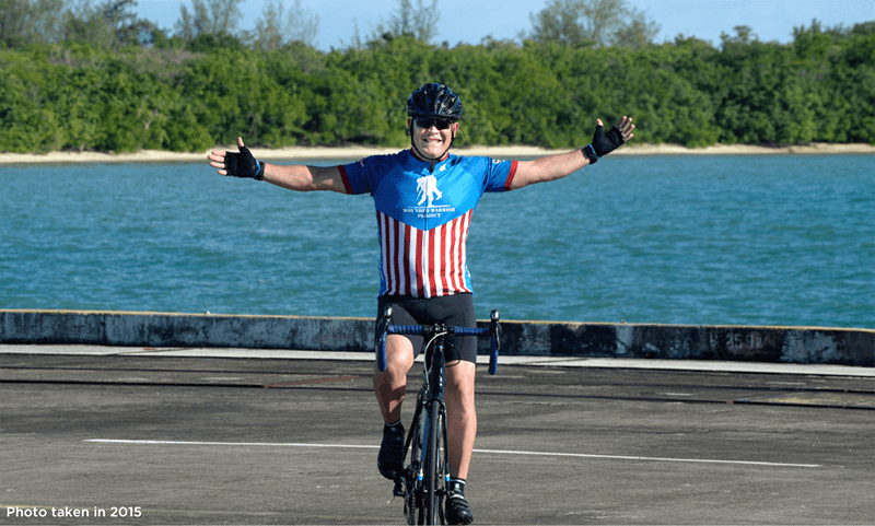 David Camacho posing on his bike with arms out wide in front of a body of water.