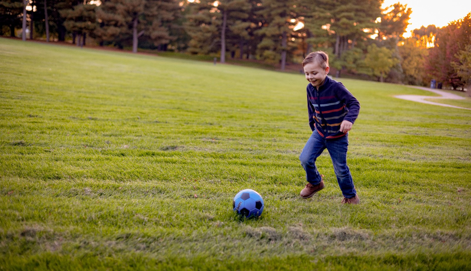 Miracle Child Benjamin kicks a blue soccer ball on a grassy field in Hershey as the sun sets